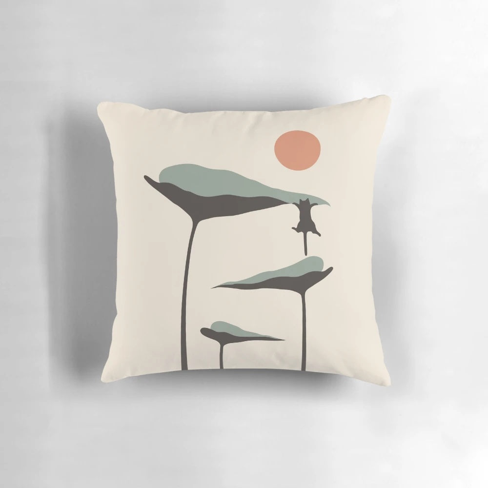 A decorative throw pillow featuring a black cat and lush green plants against a vibrant sunset landscape.