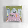 Decorative cat pillow featuring a black, tuxedo, and ginger cat lounging on a pink sofa