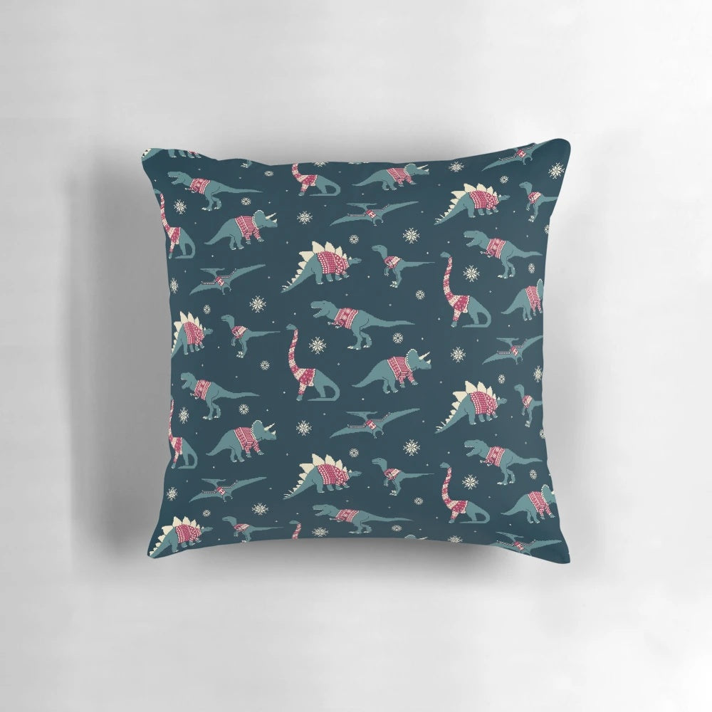 A decorative pillow featuring cute cartoon dinosaurs wearing colorful holiday sweaters.