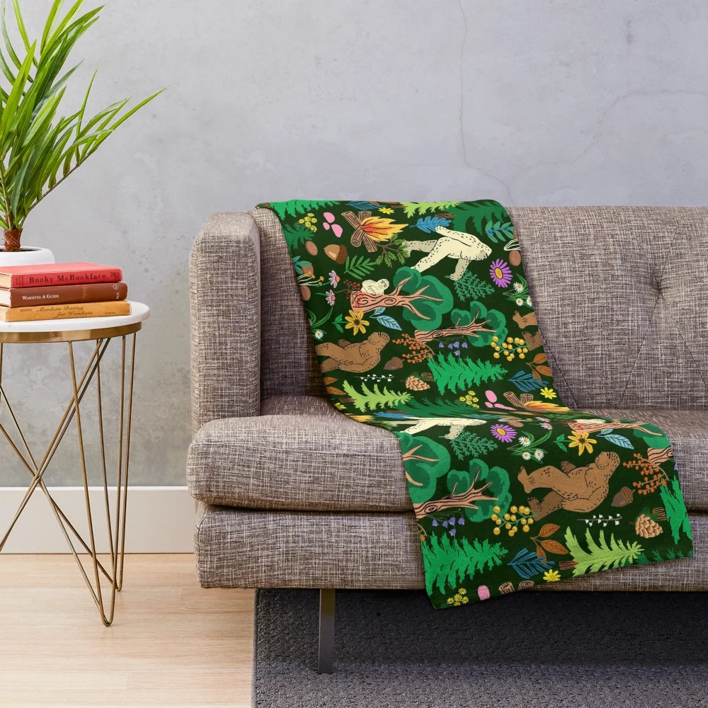 A cozy plush blanket featuring a forest scene with bigfoot, sasquatch, and other nature elements.
