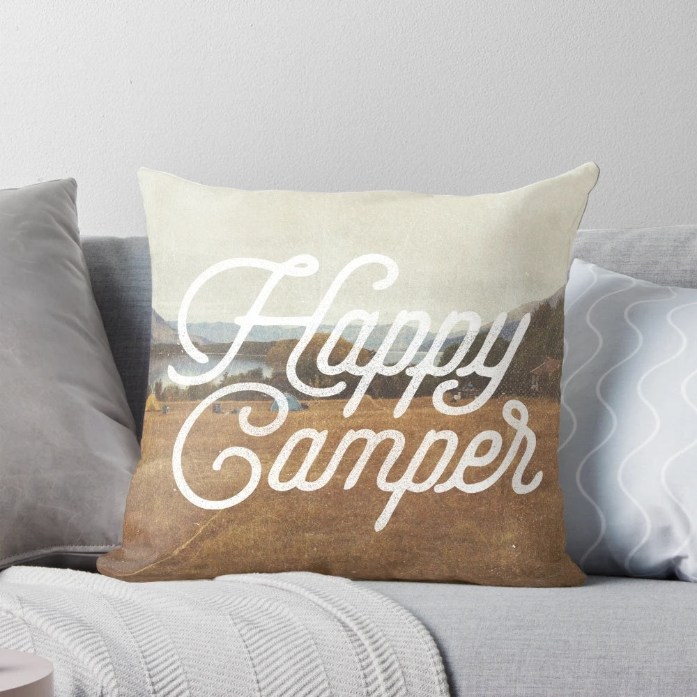 A cozy "Happy Camper" decorative pillow featuring a nature-inspired collage design with mountains, landscapes, and hiking elements.