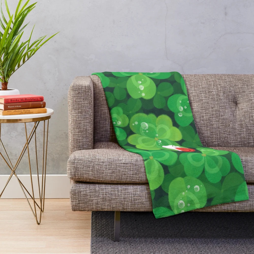 A cozy and soft plush blanket featuring a happy and lucky snail design with 4 leaf clovers and plants.