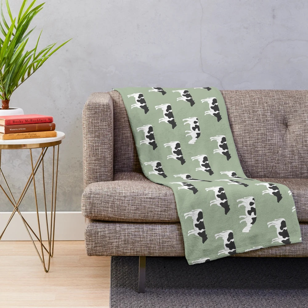 Plush blanket featuring dairy cows against a sage green background
