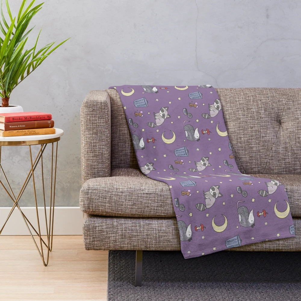 Plush blanket featuring a pattern of raccoons, opossums, and other nocturnal critters in a trash-themed design