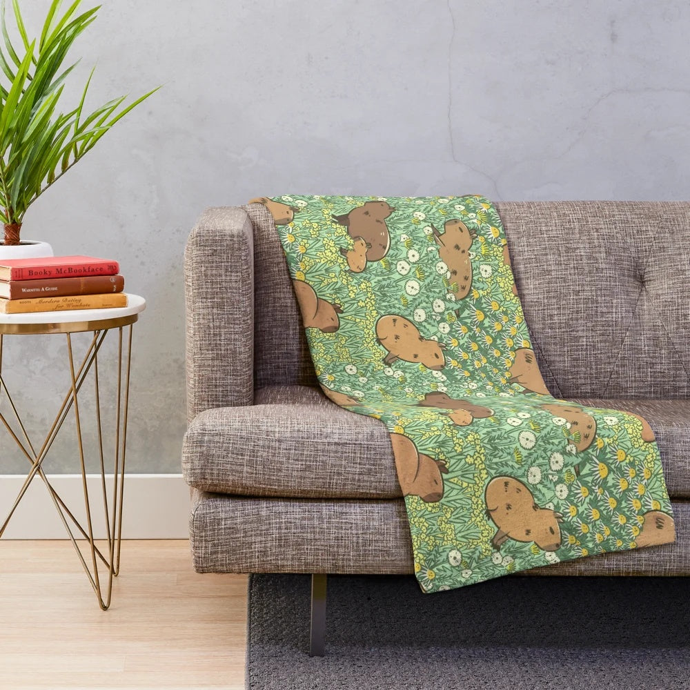 Plush blanket featuring a repeating pattern of capybaras in a lush green and yellow meadow