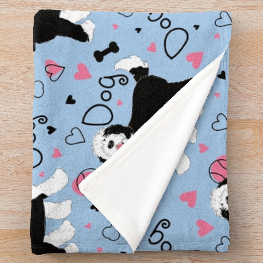 Cute black and white sheepadoodle puppy on a soft, plush blanket