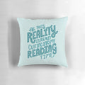 A blue and turquoise throw pillow with the text "Reality Vs. Reading" and a book nerd quote.