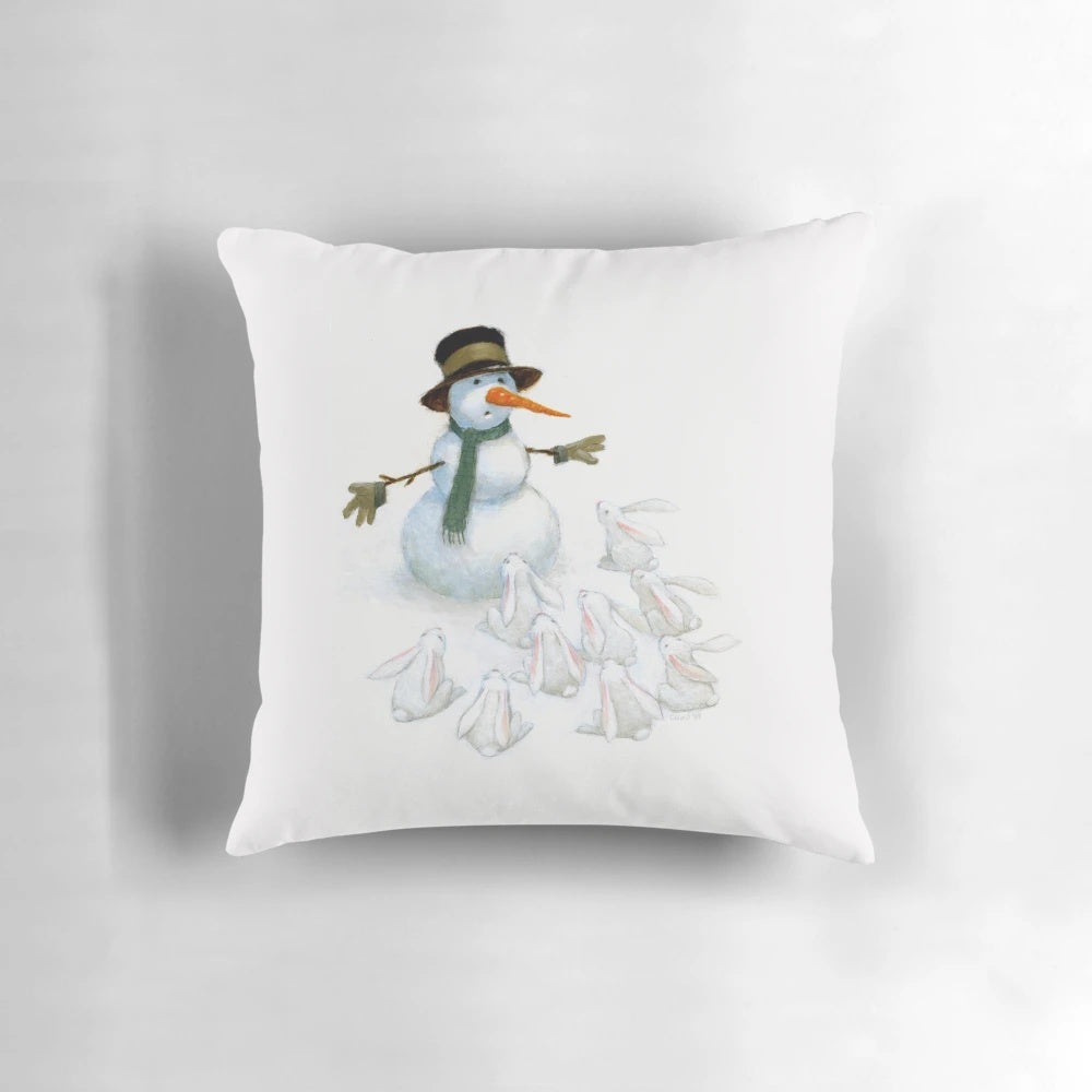 A white snowman with a carrot nose facing a group of hungry white bunnies on a soft, plush pillow.