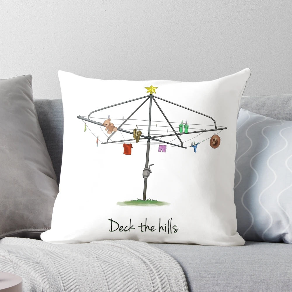 A white square pillow with a whimsical "Deck the Hills" design, featuring Australian imagery like a Hills Hoist clothesline.