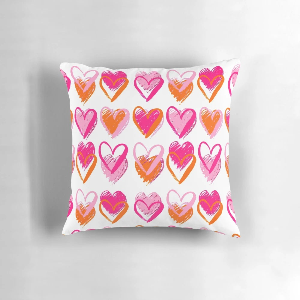 A decorative pink and orange heart-shaped pillow with a preppy, layered heart design.