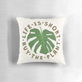 A decorative throw pillow featuring the whimsical message "Life is Short, Buy the Plant" against a lush, tropical plant background.
