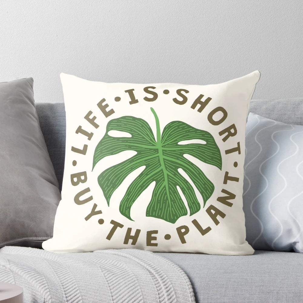A decorative throw pillow featuring the whimsical message "Life is Short, Buy the Plant" against a lush, tropical plant background.