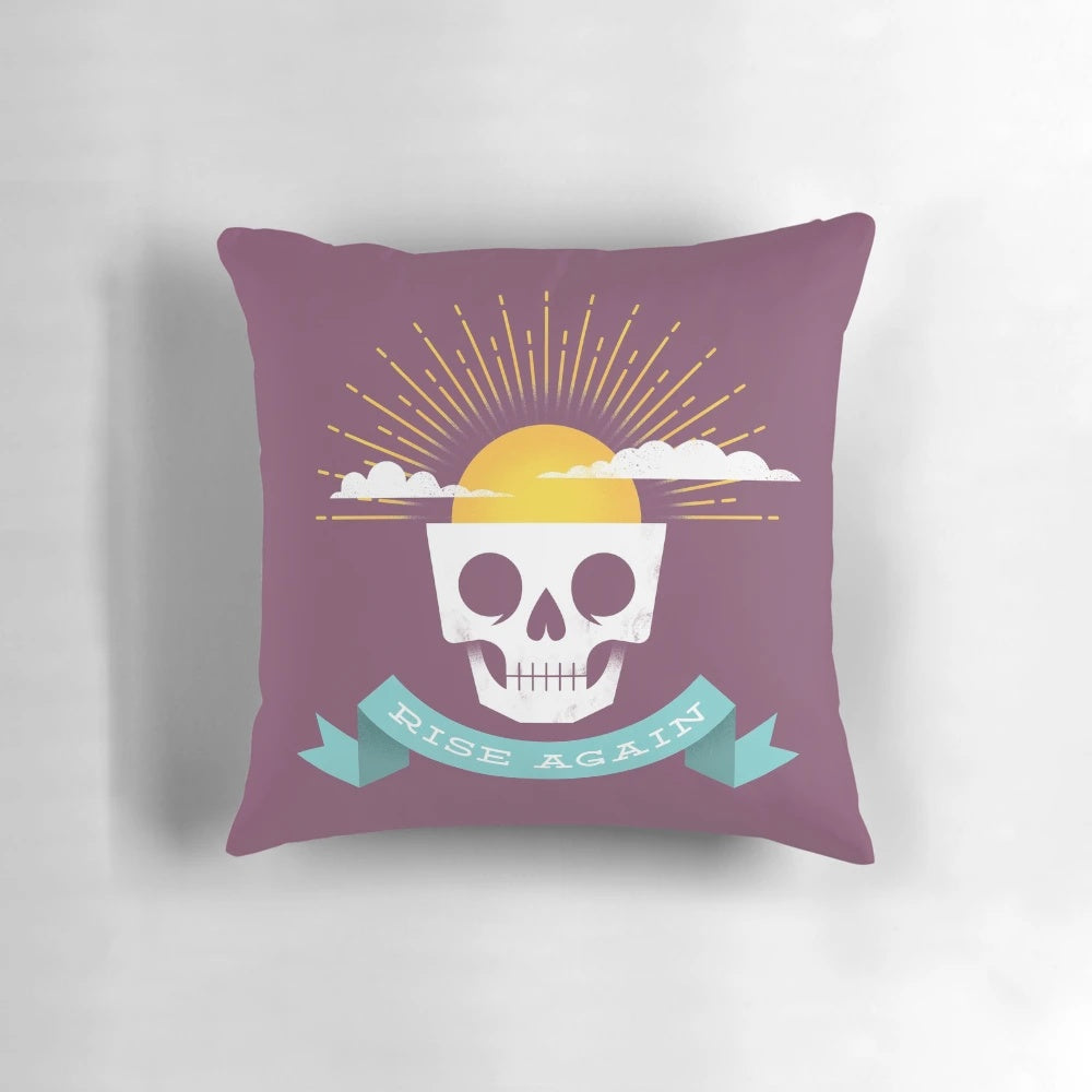 Rise Again Pillow featuring a sun rising over a skull, symbolizing new life and optimism.