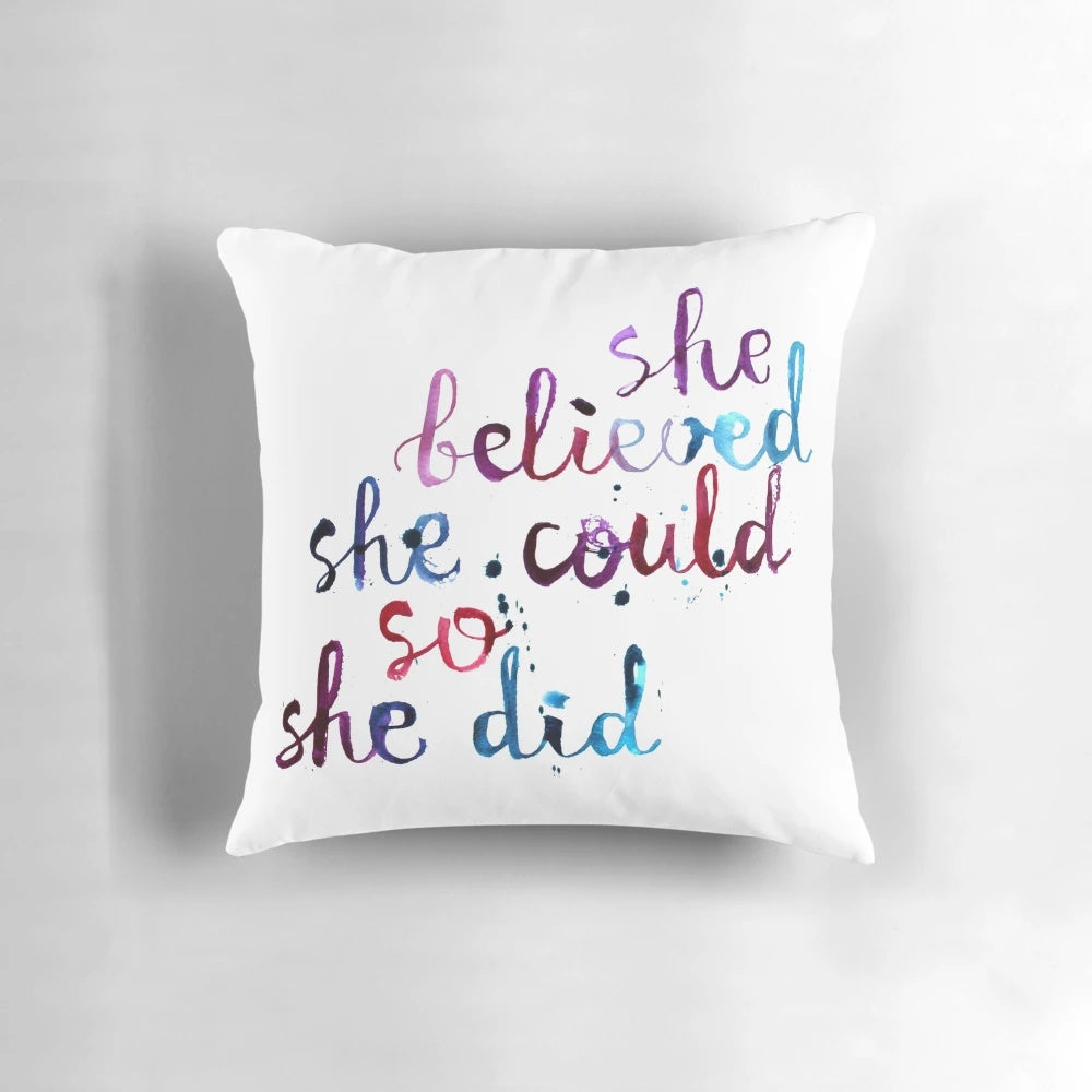 Decorative pillow with the motivational quote "She believed she could so she did" in calligraphic typography and watercolor design.