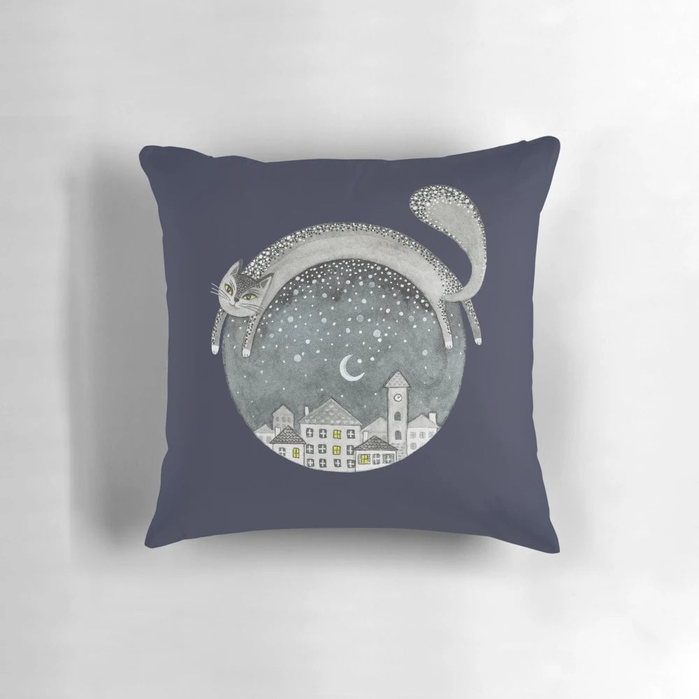 Cozy pillow featuring a whimsical cat in a night town scene with the moon, stars, and houses.