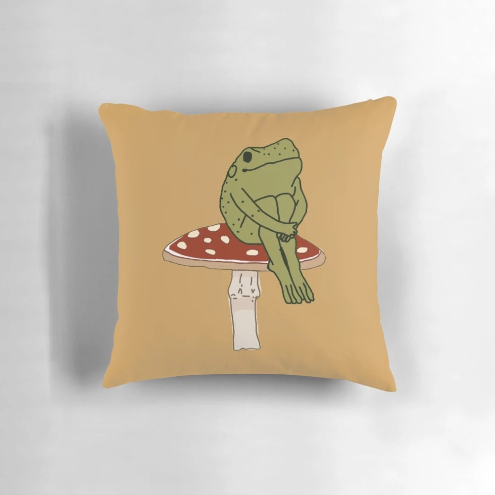 A whimsical pillow featuring a charming green frog sitting on a cottagecore-inspired mushroom.