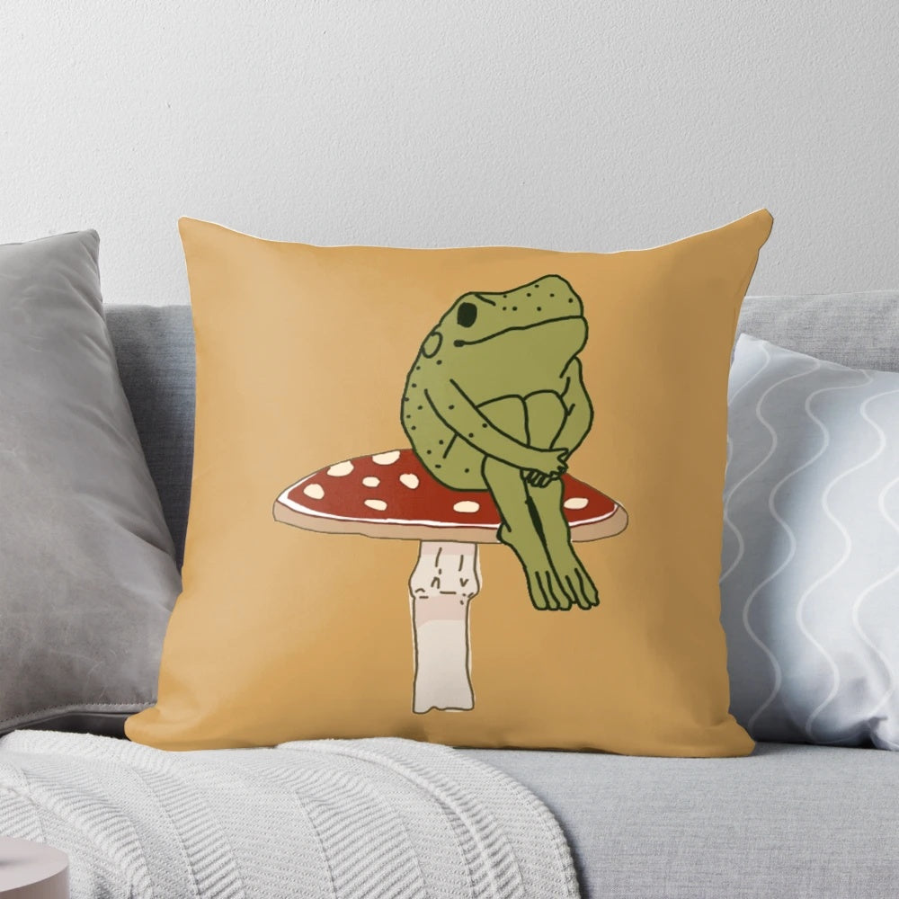 A whimsical pillow featuring a charming green frog sitting on a cottagecore-inspired mushroom.