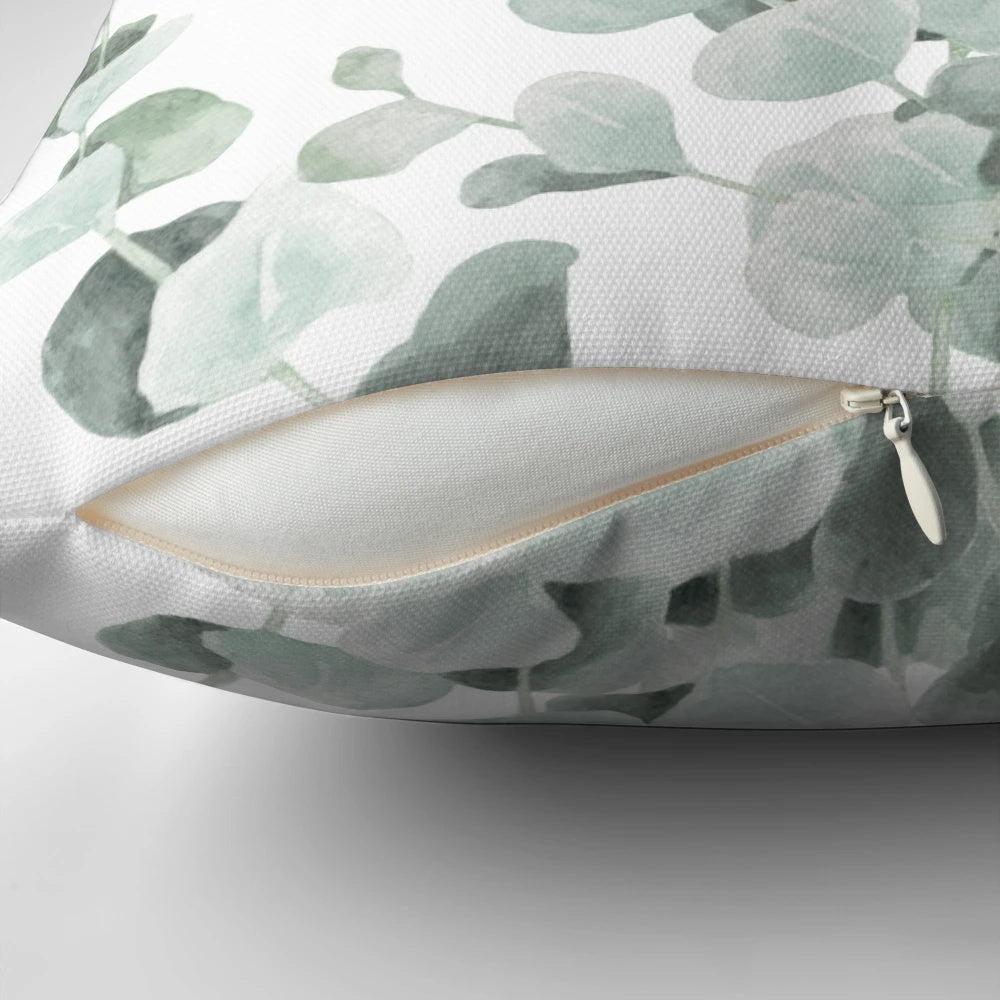 A decorative pillow featuring a watercolor illustration of standing eucalyptus leaves in shades of teal and sage.