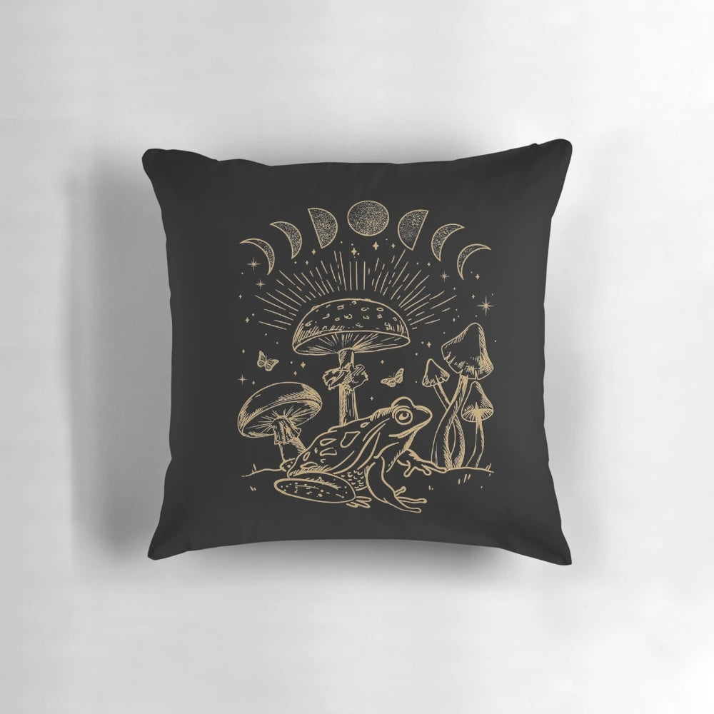 A decorative pillow featuring a frog under a mushroom, with a dark academia, cottagecore, and goth-inspired design.