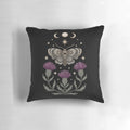 Decorative pillow featuring a moth and thistle design against a crescent moon backdrop