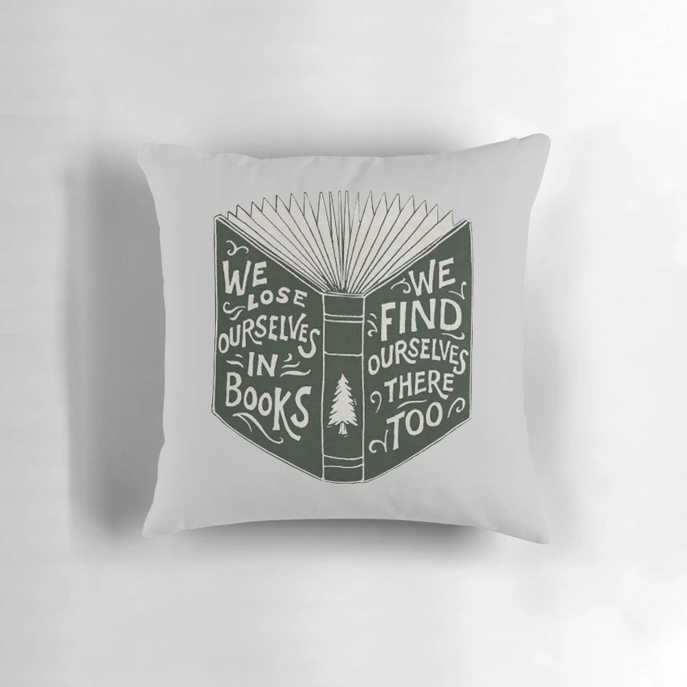 A soft, plush pillow with a design featuring an open book and the words "We Lose Ourselves in Books...