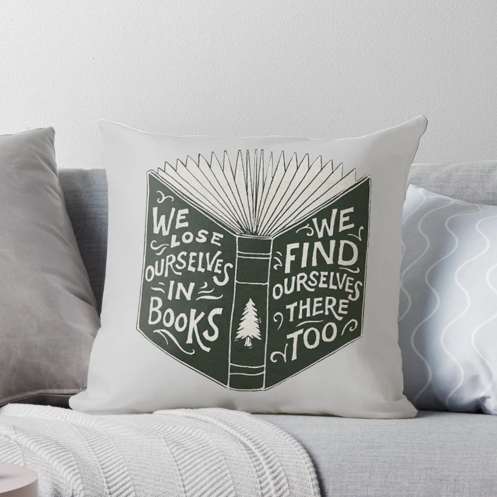 A soft, plush pillow with a design featuring an open book and the words "We Lose Ourselves in Books...
