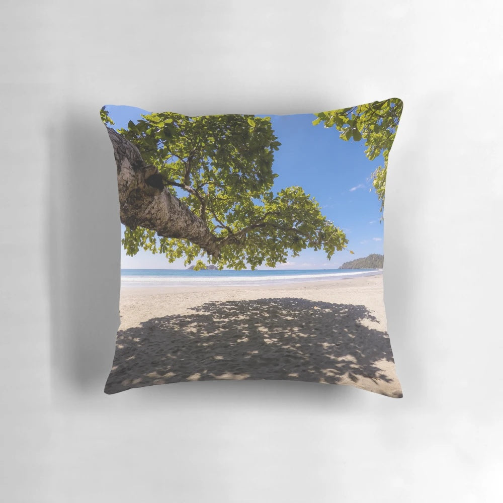 A shady spot on a tropical beach pillow, featuring lush greenery and a serene ocean view.