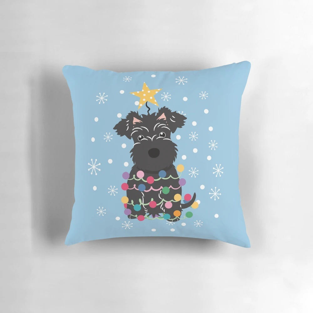 A fluffy black miniature schnauzer dog sitting on a Christmas tree-shaped pillow.