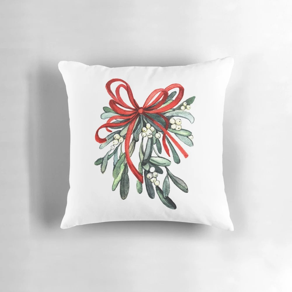 A decorative pillow featuring a branch of green mistletoe with white berries, a classic symbol of the holiday season.