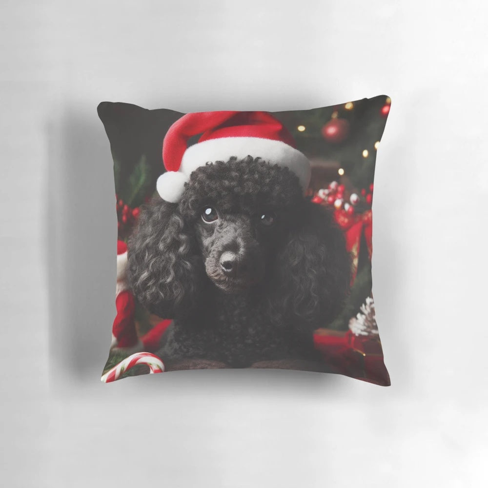 A black miniature poodle wearing a Santa hat on a Christmas-themed decorative pillow.