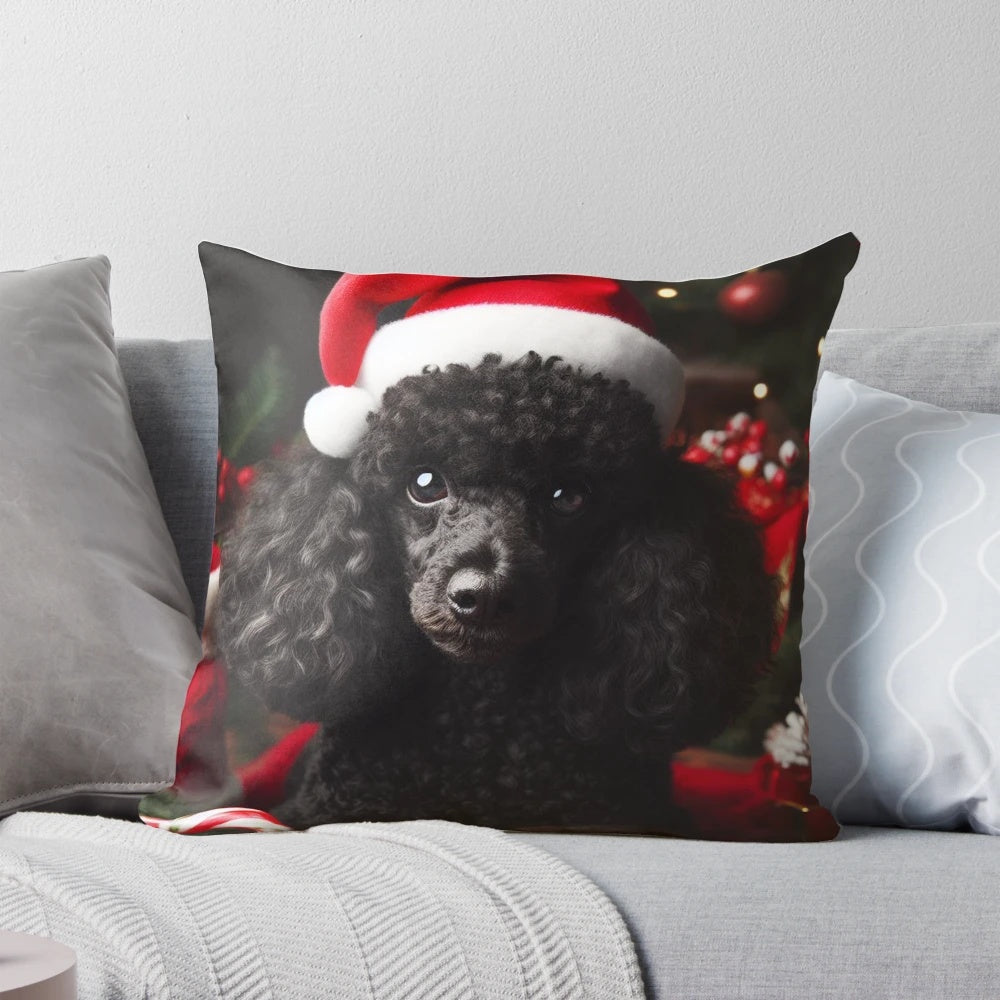 A black miniature poodle wearing a Santa hat on a Christmas-themed decorative pillow.