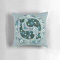 A decorative throw pillow featuring a floral and whale design in shades of blue and green.
