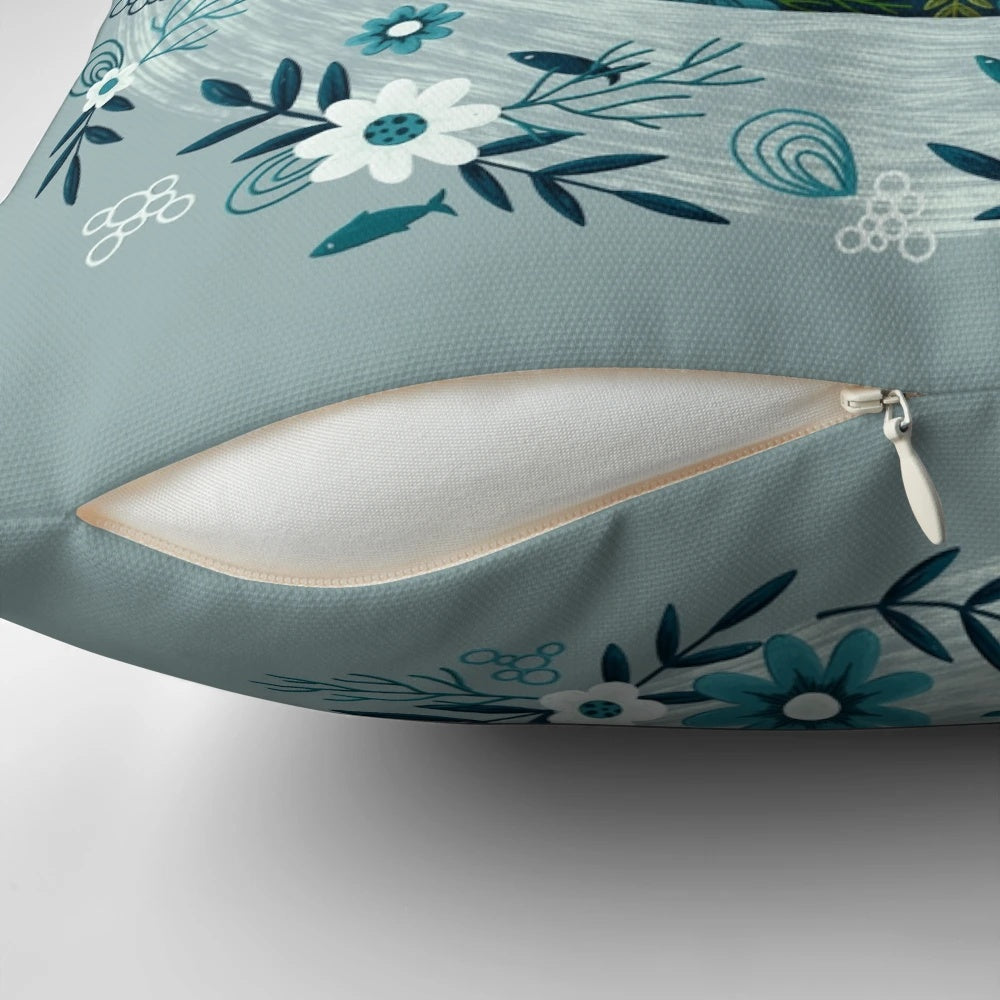 A decorative throw pillow featuring a floral and whale design in shades of blue and green.