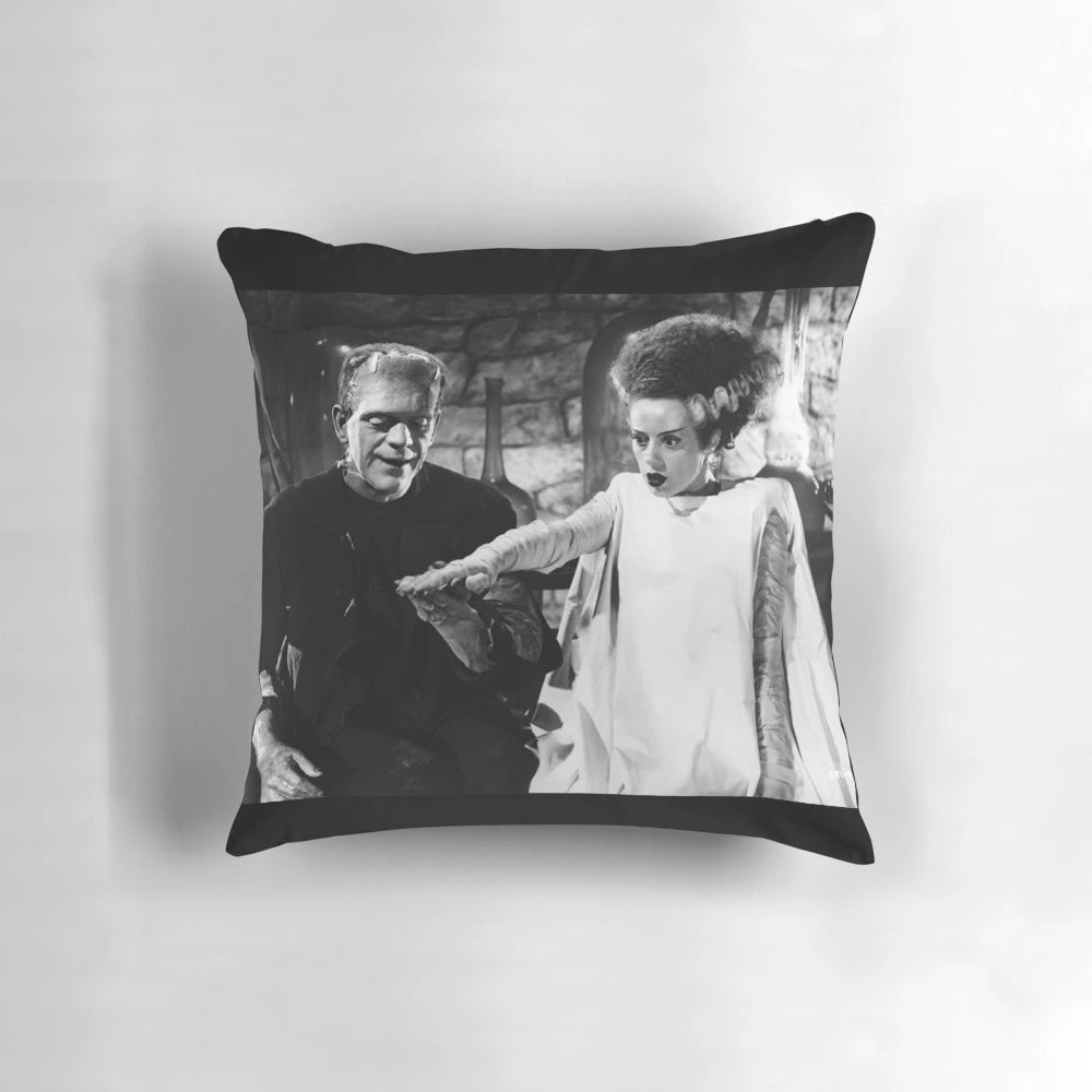 Frankenstein and his bride holding hands on a decorative throw pillow