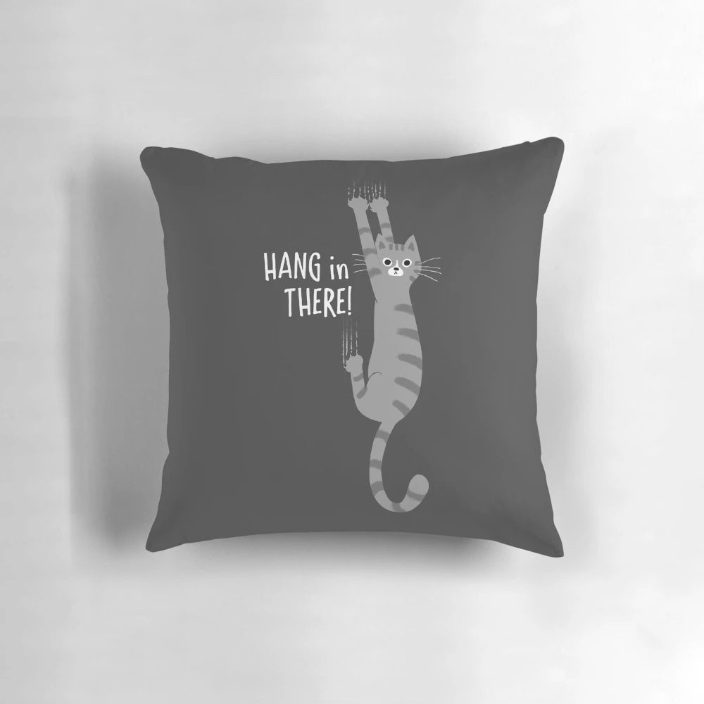 Gray striped tabby cat hanging on a pillow with the text "Hang in There!