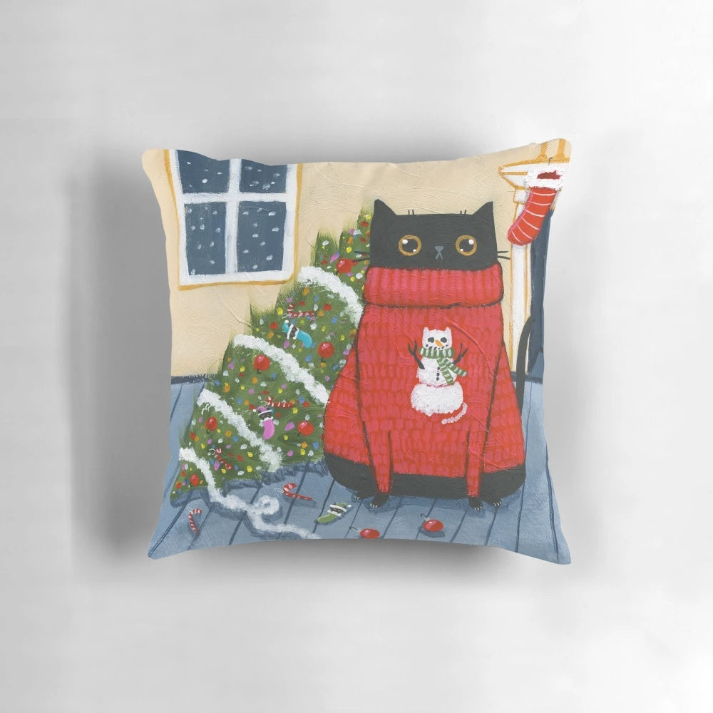 A black cat with an "It Wasn't Me" expression knocks over a Christmas tree on a plush pillow