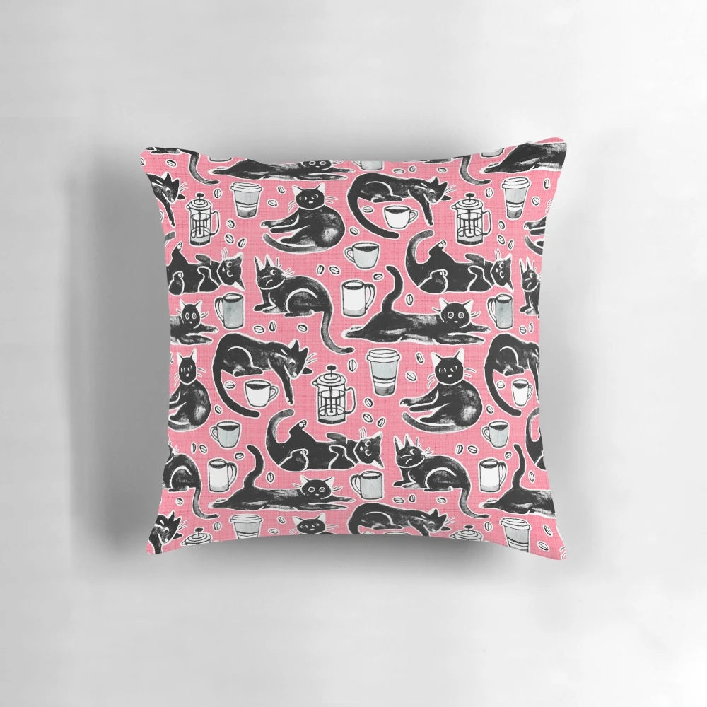 A decorative pillow featuring a hand-painted pattern of black cats on a strawberry pink background.