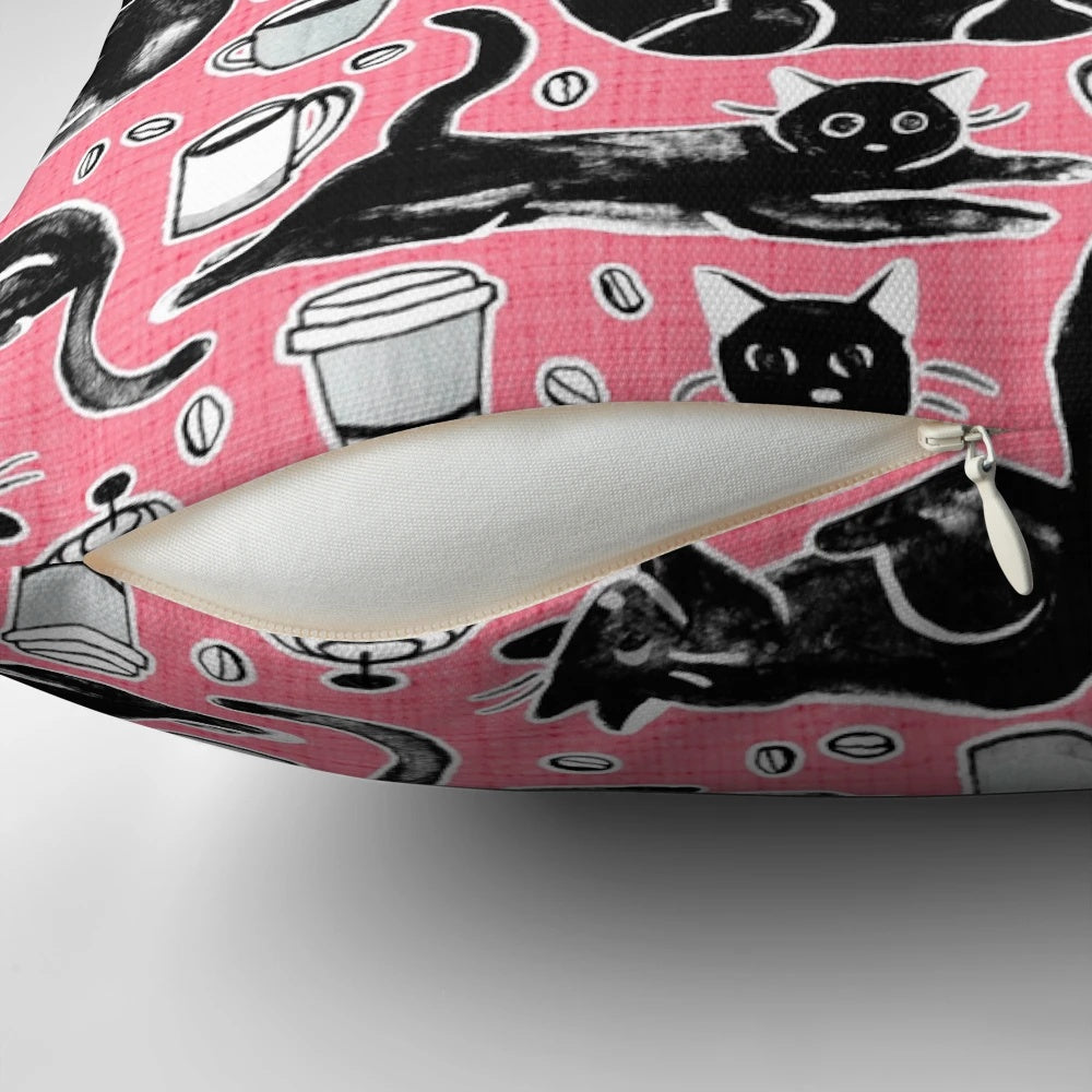 A decorative pillow featuring a hand-painted pattern of black cats on a strawberry pink background.
