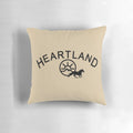 A black pillow with the Heartland TV show logo, featuring horses and the Montana landscape.