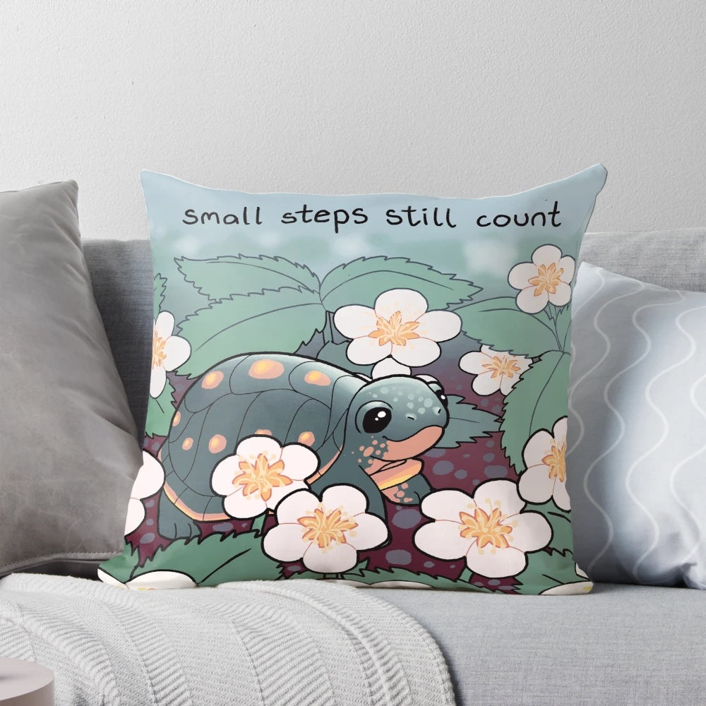 A soft, square pillow with an illustration of a baby turtle surrounded by strawberry flowers, with the text "Small Steps Still Count