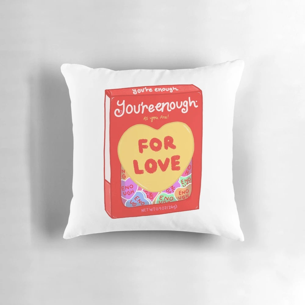 A pink and white 'You're Enough' throw pillow with a whimsical, artsy design to promote mental health and self-love.