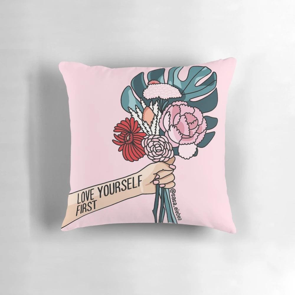 A white pillow with a pink floral pattern and the text "Love yourself first" printed on it.