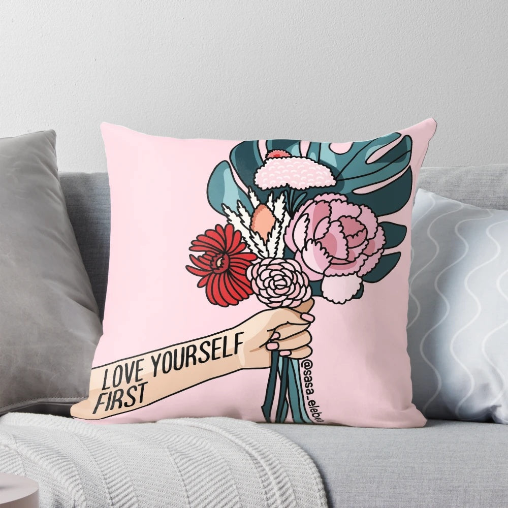 A white pillow with a pink floral pattern and the text "Love yourself first" printed on it.