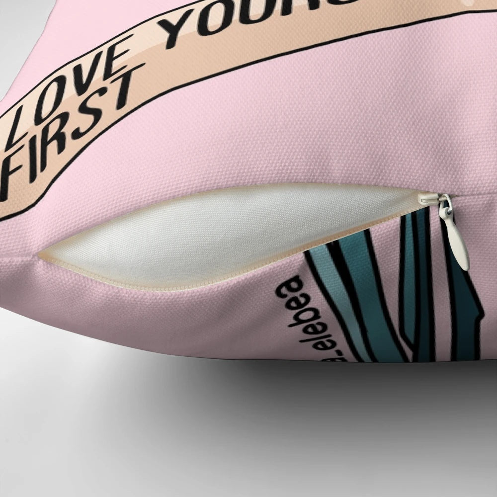 A white pillow with a pink floral pattern and the text "Love yourself first" printed on it.