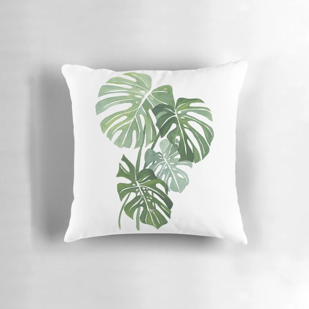 Vibrant watercolor illustration of lush monstera leaves printed on a plush, throw pillow for indoor botanical home decor.