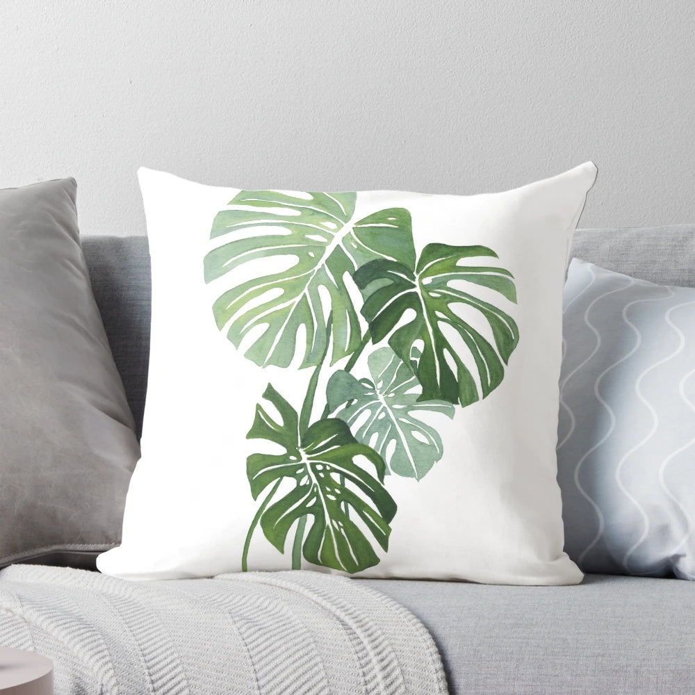Vibrant watercolor illustration of lush monstera leaves printed on a plush, throw pillow for indoor botanical home decor.