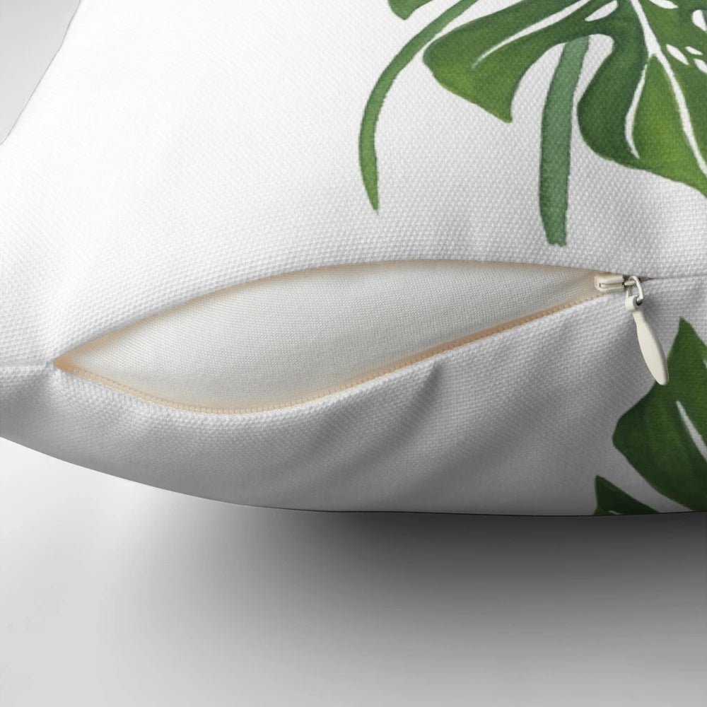 Vibrant watercolor illustration of lush monstera leaves printed on a plush, throw pillow for indoor botanical home decor.