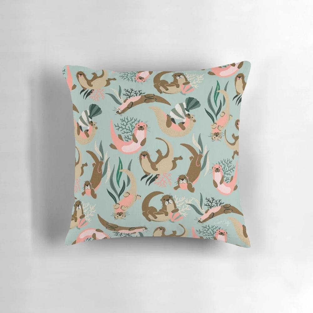 A mint-colored decorative pillow featuring adorable otters swimming in the ocean.