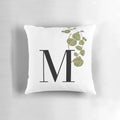 A square decorative throw pillow featuring a green plant motif design in the shape of the letter M.