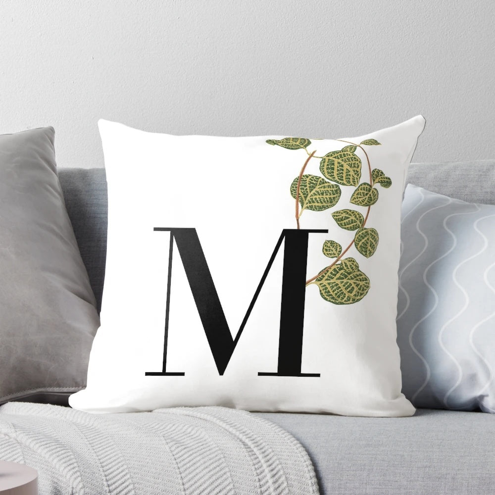 A square decorative throw pillow featuring a green plant motif design in the shape of the letter M.